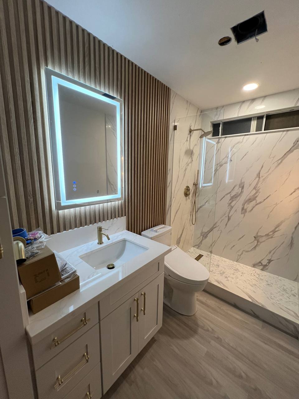 Marble-look walk-in shower with backlit mirror and brass fixtures, after